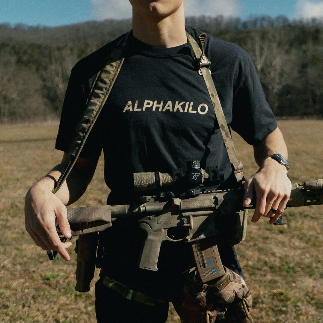 Person wearing an AlphaKilo shirt with tactical gear in a field