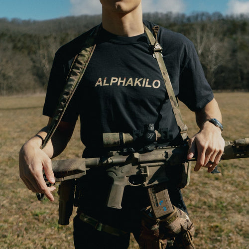 Person wearing an AlphaKilo shirt with tactical gear in a field