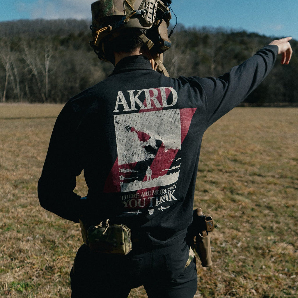 Person in tactical gear pointing into the distance with 'AKRD' branding on clothing